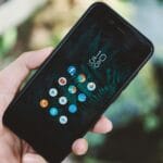 Dłoń trzymająca smartfon z ikonami aplikacji na tle natury