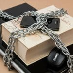 Zeszyt, telefon i laptop oplecione łańcuchem jako symbol ochrony danych