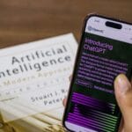 Smartfon z otwartą aplikacją ChatGPT trzymany nad podręcznikiem o AI