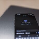 Zbliżenie smartfona z interfejsem asystenta AI na ekranie nad laptopem