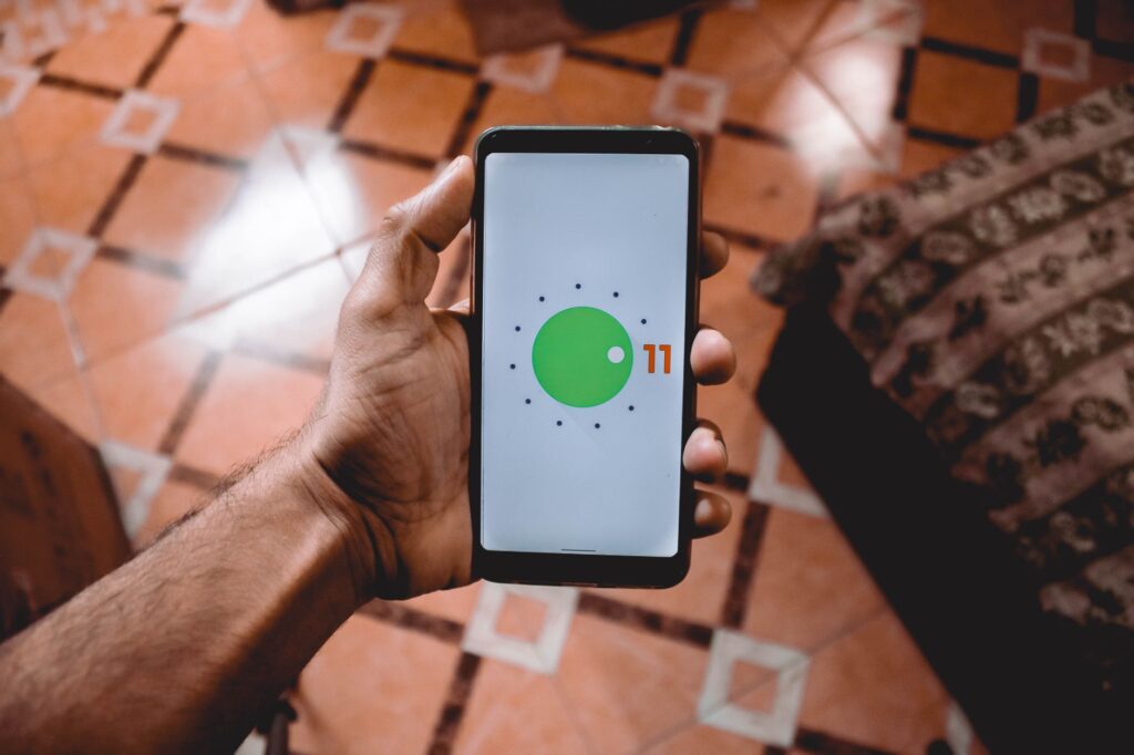 Dłoń trzymająca smartfon z interfejsem Android 11